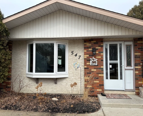 The front of a house with a custom bay window installed by Hi-Tech. The window has a solid frame and 3 panes of glass. It overhangs a garden.