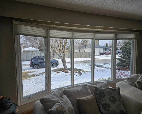 Interior view of a new living room bow window installed by Hi-Tech. It has five gently-angled panes of glass and custom blinds, one for each pane.